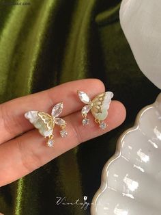 a hand holding two small white and gold earrings