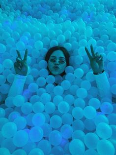 a woman is floating in the water surrounded by balls with her hands up and two fingers out