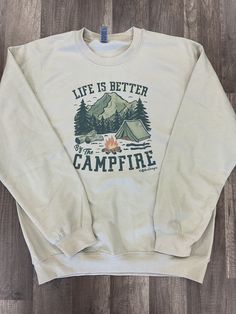 Tan sweatshirt with a camp fire scene that says “LIFE IS BETTER BY THE CAMPFIRE” Summer Camp Merch, Campfire Sweatshirt, Fall Camping Outfits, Camping Attire, Camping Clothes, Fire Clothes, Projets Cricut, Fall Camping