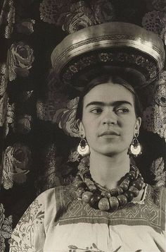 a black and white photo of a woman with jewelry on her head in front of a wall