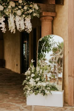 a large mirror sitting on top of a white box next to a flower filled wall