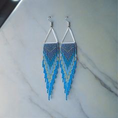 two pairs of blue and green beaded earrings on a marble counter with white background