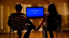 two people sitting in chairs facing each other with a television on the wall behind them