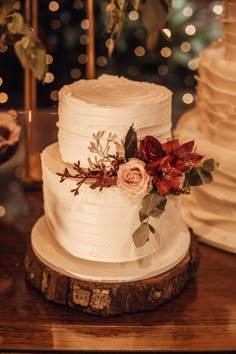 a white wedding cake with red flowers and greenery sits on a wooden stand in front of a christmas tree