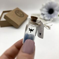 a hand holding a tiny glass bottle with a bird on it