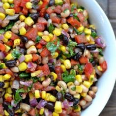 a white bowl filled with corn and black bean salad on top of a wooden table