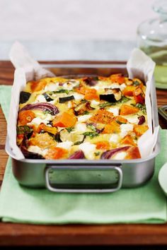 a casserole dish with vegetables in it on a wooden tray next to spoons and utensils