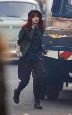 a woman with red hair is walking down the street in front of a garbage truck