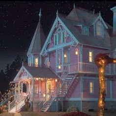 a large pink house with christmas lights on it's front porch and steps leading up to the upper level