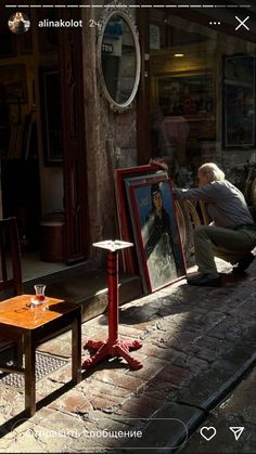 a man sitting on a bench in front of a table with a painting next to it