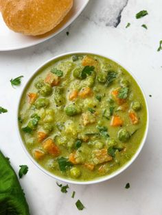 a bowl of green soup next to a plate of bread