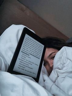 a woman laying in bed under a blanket with an electronic book on her lap,