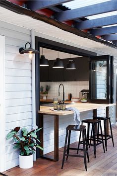 an outdoor kitchen with bar stools next to it and a potted plant on the counter