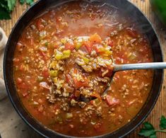 a ladle full of soup with meat and vegetables in it on a wooden table