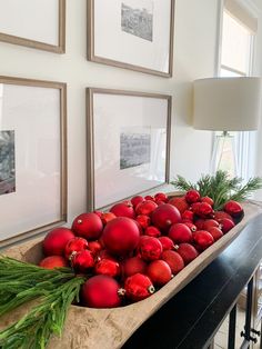 christmas ornaments in a wooden bowl on a table next to framed pictures and a lamp