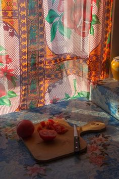 a cutting board with some tomatoes on it next to a window covered in sheer curtains