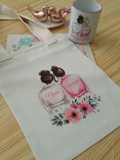 a white bag with two women's perfume bottles on it next to a coffee mug