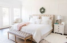 a bedroom with white walls and carpeted flooring has a large bed, two nightstands, and a bench in front of the bed