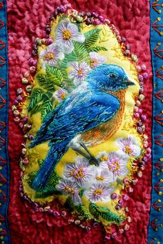 a blue bird sitting on top of a red and yellow pillow with flowers around it