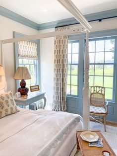 a white bed sitting in a bedroom next to a window covered in curtains and pillows