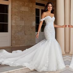 a woman in a white wedding dress standing on some steps with her arms out to the side