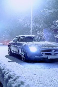 a mercedes sls driving down a snowy road in front of some snow covered trees