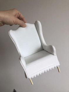 a hand is holding a miniature white chair