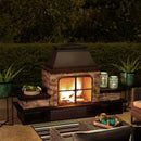 an outdoor fireplace lit up at night with potted plants