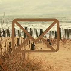 an email envelope sitting in the sand by the beach with sea oats behind it