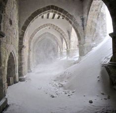 snow is covering the ground in an old stone building with arched doorways and arches