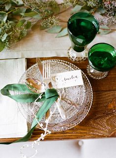 a place setting with green glassware and greenery