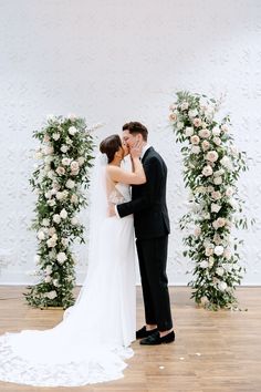 a bride and groom kissing in front of an arch of flowers on the dance floor