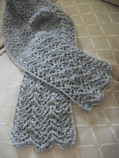 a crocheted gray scarf laying on top of a white bed cover with pillows