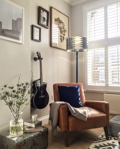 a living room with a guitar on the wall next to a chair and vase filled with flowers