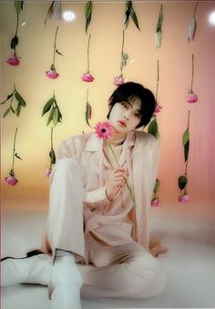 a woman sitting on the ground with flowers in her hair and holding a pink flower