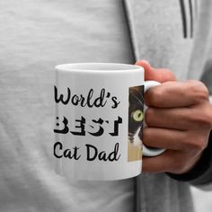 a person holding a coffee mug with a cat on it's side and the words world's best cat dad