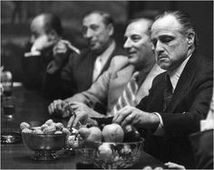 black and white photograph of men sitting at a table with bowls of fruit in front of them