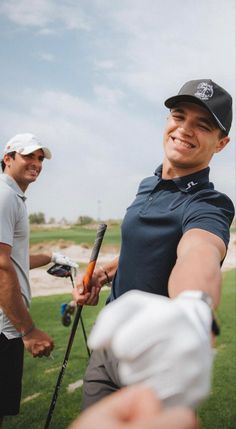 two men holding golf clubs and smiling at the camera while one holds his arm out