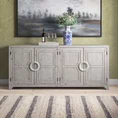 a painting hanging on the wall above a sideboard with wine glasses and vases