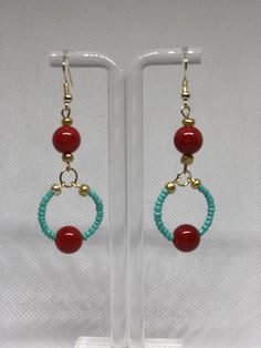 a pair of earrings with red beads and turquoise beaded hoops on a white stand