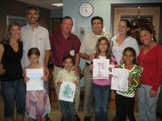 a group of people standing next to each other holding up pictures and smiling at the camera