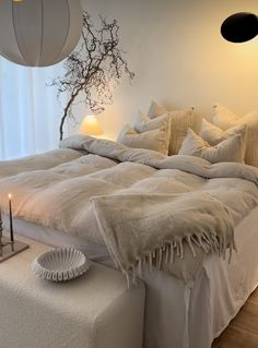 a bed with white linens and pillows in a bedroom next to a tree branch