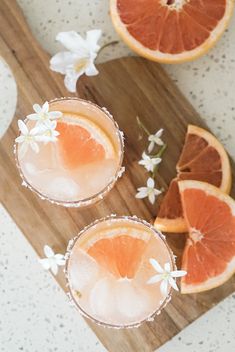 two grapefruit margaritas with orange slices and flowers on a wooden cutting board