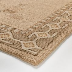 a beige rug with an intricate design on the top and bottom corner, is laying on a white surface