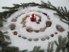 a candle is surrounded by rocks and pine needles in the middle of a snow - covered circle