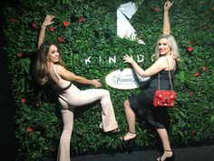 two beautiful women standing next to each other near a wall covered in plants and flowers