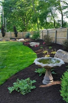 a bird bath sitting in the middle of a lush green yard next to a wooden fence