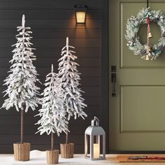 three white christmas trees sitting in front of a door