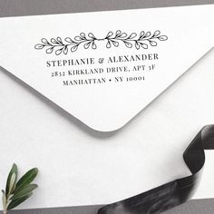 an envelope with a black and white address stamp on it, next to a plant