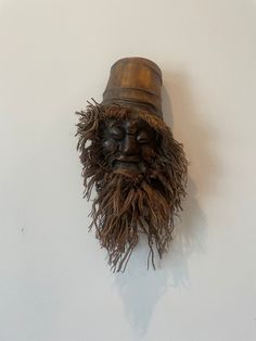 a wooden mask hanging on the wall with a hat on it's head and beard